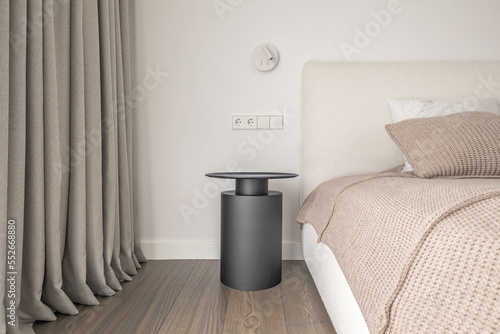 White wall lamp above the bed, metal beside table, white electrical outlet, oak wooden floor..Modern minimalist aesthetic bedroom interior design in warm shades