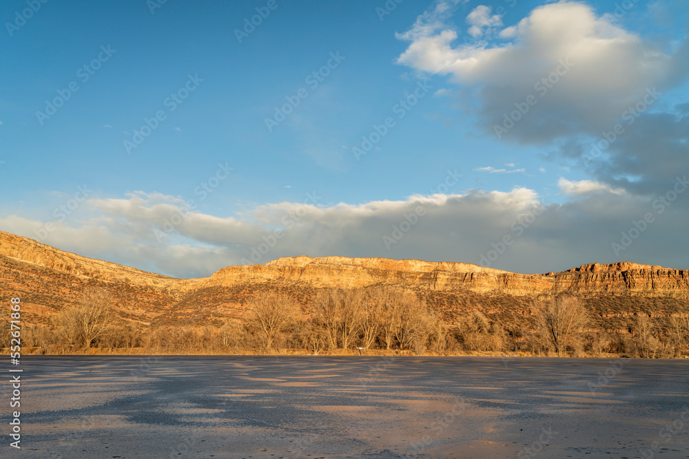 sunset light over a frozen lake and sandstone cliff at Colorado foothills of Rocky Mountains