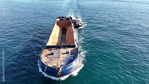 Aerial drone video of assisted with tug boat empty barge boat cruising in deep blue sea photo