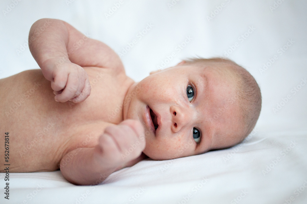 A cute little baby lies on the bed. Cute little baby smiling. Newborn baby on white background A cute little baby lies on the bed. Cute little baby smiling. Newborn baby on white background