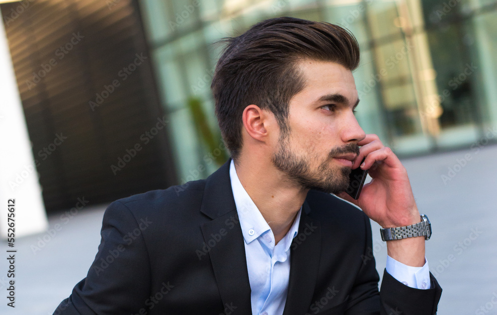 Young businessman sitting in front of corporate office building and using smart phone Young businessman sitting in front of corporate office building and using smart phone