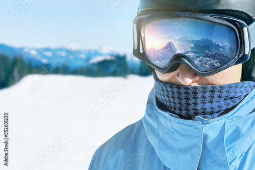 Zamyka up narciarskie gogle mężczyzna z odbiciem zaśnieżone góry. Pasmo górskie odbite w masce narciarskiej. Mężczyzna na tła niebieskim niebie. Noszenie okularów narciarskich. Sporty zimowe.