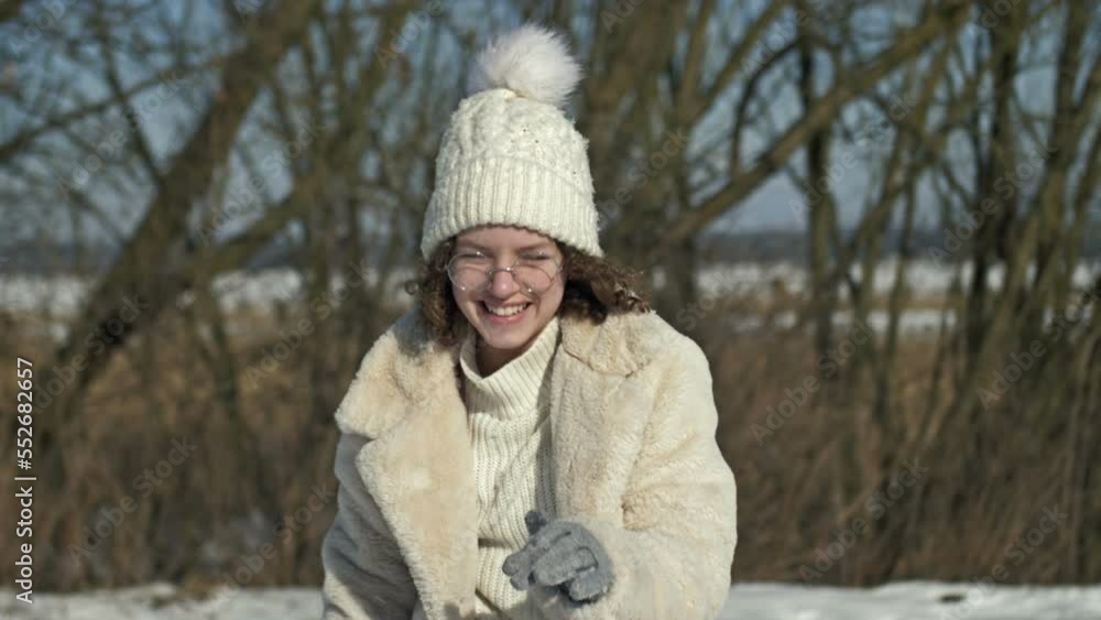 Cheerful teenage girl in a white knitted cap and glasses throws a snowball. Cheerful teenage girl in a white knitted cap and glasses throws a snowball.