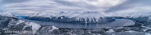 Panoramic aerial image of Tutshi Lake on a grey day with dramatic clouds with snow capped mountains in winter; Yukon, Canada