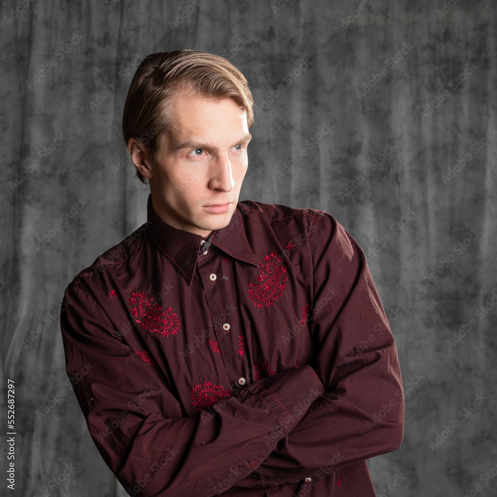 Obraz premium an attractive man in an elegant suit, burgundy shirt with embroidery. Photo in the studio on a gray background