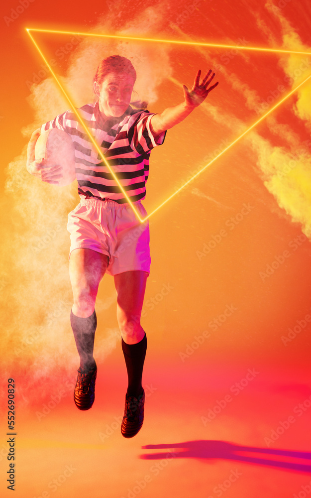 Caucasian woman jumping with ball by illuminated triangle and smoke on orange background