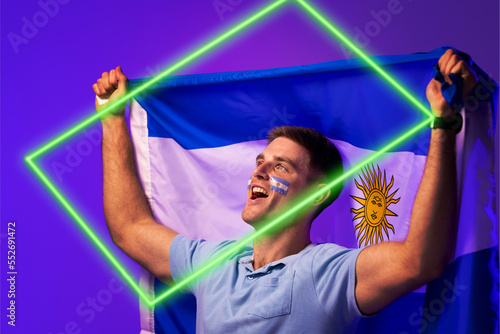 Caucasian male fan with argentina national flag and face paint screaming by illuminated rectangle
