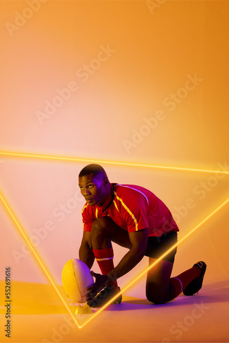 Confident african american male rugby player placing ball on stand by illuminated triangle