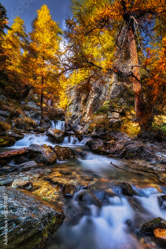 Long exposure of little waterfalls stream in the beautiful Vallée Étroite, during the autumn larches foliage, France