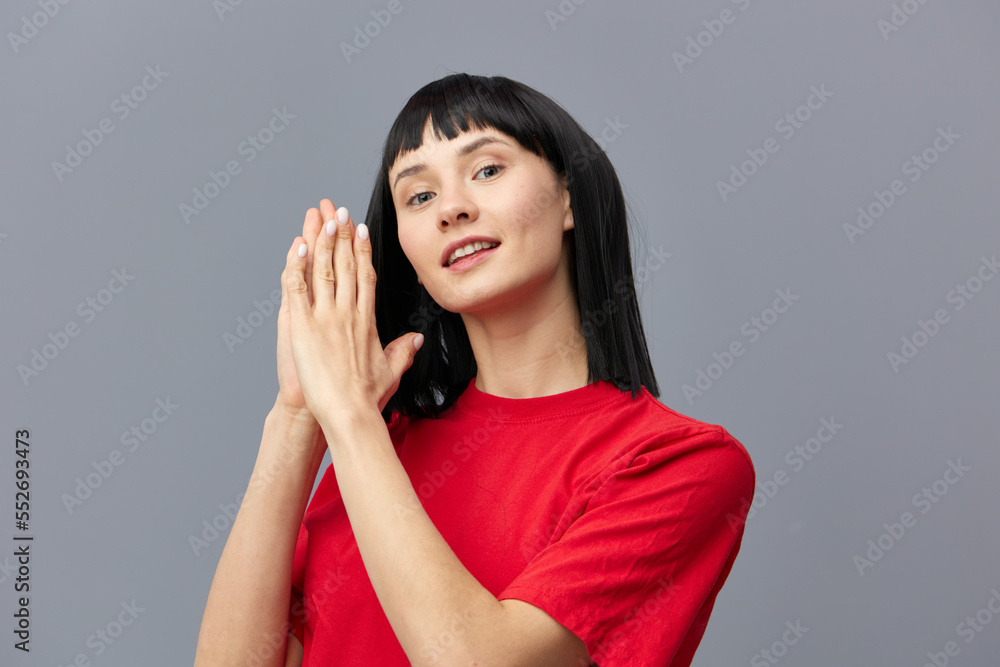 a sweet, gentle, sophisticated, relaxed woman with black hair stands in a red T-shirt on a gray background and holds her hands near her face a sweet, gentle, sophisticated, relaxed woman with black hair stands in a red T-shirt on a gray background and holds her hands near her face