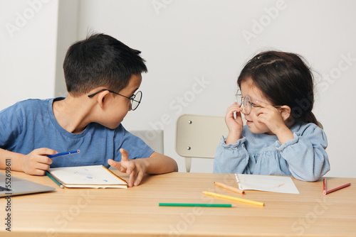 little children brother and sister sit at a desk and draw with pencils