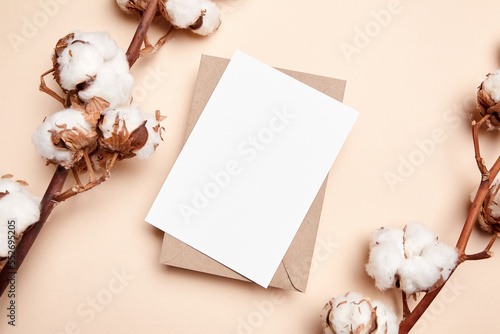 Holiday greeting card mockup with dried branch of cotton flowers and envelop on beige background, top view, flat lay. White wedding invitation card mock up © mikeosphoto