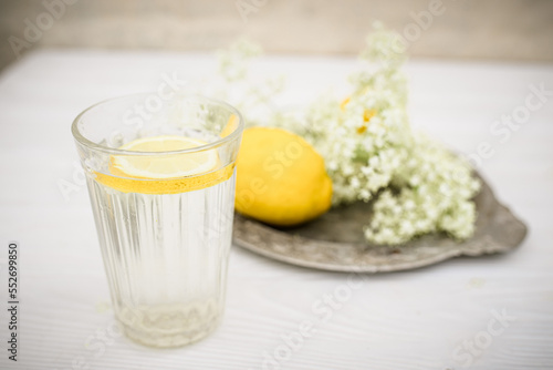 Cold lemonade with elderberry syrup and lemon in faceted glass on table near a freshly cut branch of flowering elderberry. Summer refreshing drink or non-alcoholic cocktail used in physiotherapy photo