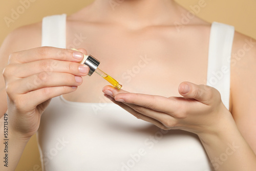 Young woman applying essential oil onto hand on beige background  closeup