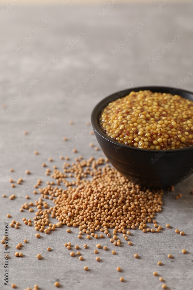 Bowl of whole grain mustard and seeds on grey table, closeup Bowl of whole grain mustard and seeds on grey table, closeup