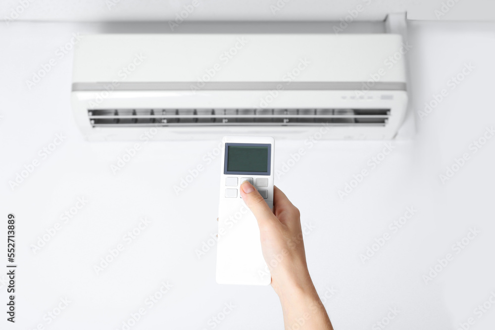 Woman operating air conditioner with remote control indoors, closeup Woman operating air conditioner with remote control indoors, closeup