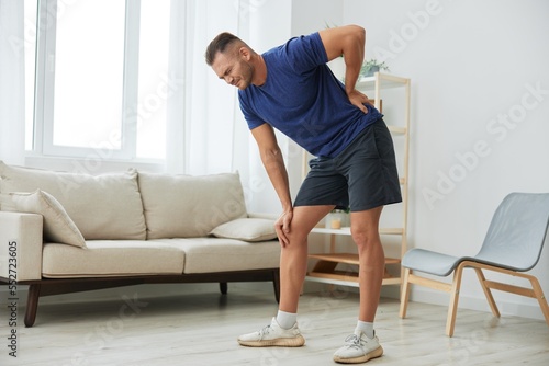 Man backache neck and shoulder pain, inflammation of muscles and ligaments rupture during sports, inflammation and injury, in a blue t-shirt at home © SHOTPRIME STUDIO