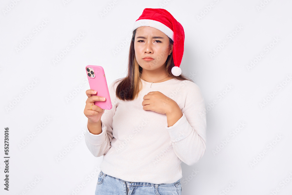 Pensive young Asian woman in a Christmas hat holding mobile phone and holding chest isolated on white background. celebration Christmas holiday and New Year concept Pensive young Asian woman in a Christmas hat holding mobile phone and holding chest isolated on white background. celebration Christmas holiday and New Year concept