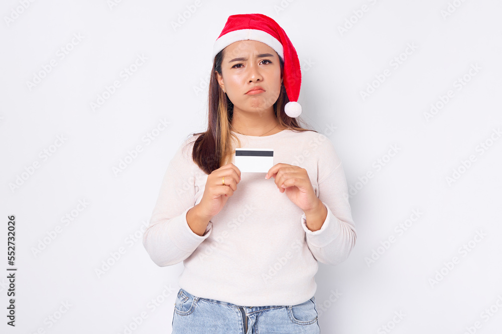 Pensive young Asian woman in a Christmas hat showing blank white credit card isolated on white background Pensive young Asian woman in a Christmas hat showing blank white credit card isolated on white background