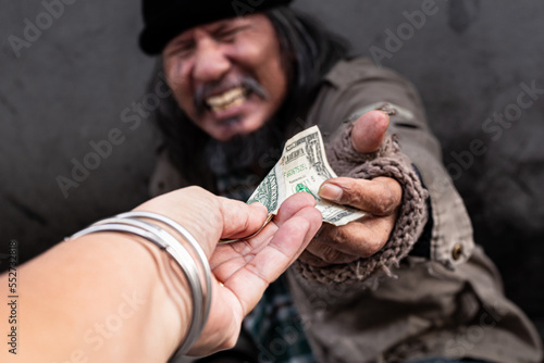 Selective focus of hand kind person giving one dollar bill money to old man homeless. Asian beggar feel happy and crying  receives money from a passerby to help. Poverty and social issue concept.