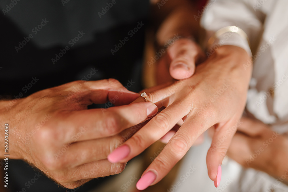 Fototapeta premium Man in love putting an engagement ring on woman finger. Propose. Closeup hands. Offer of hand and heart. Man holding his girl's hand - Man making a marriage proposal to his girlfriend. Engaged couple.