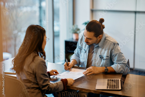 Εκτύπωση καμβά Young Hispanic man signing loan agreement during meeting with his bank manager in office