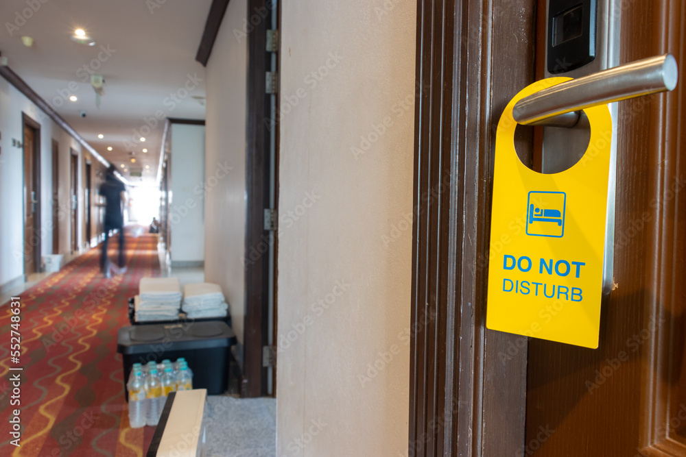 The sign Do Not Disturb hangs on the doorknob of the hotel room with blurred people on a corridor The sign Do Not Disturb hangs on the doorknob of the hotel room with blurred people on a corridor