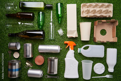 A selection of garbage for recycling. Segregated glass, metal, plastic and paper on green grass background.
