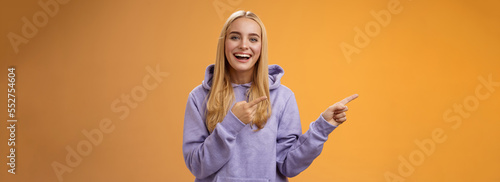 Charismatic firendly good-looking blond young female student pointing left discussing awesome new restaurant suggesting friend go check out laughing smiling happily, orange background photo