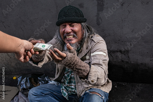 Фотография Selective focus of Asian homeless man feel happy and crying receives one dollar bill money from a passerby to help