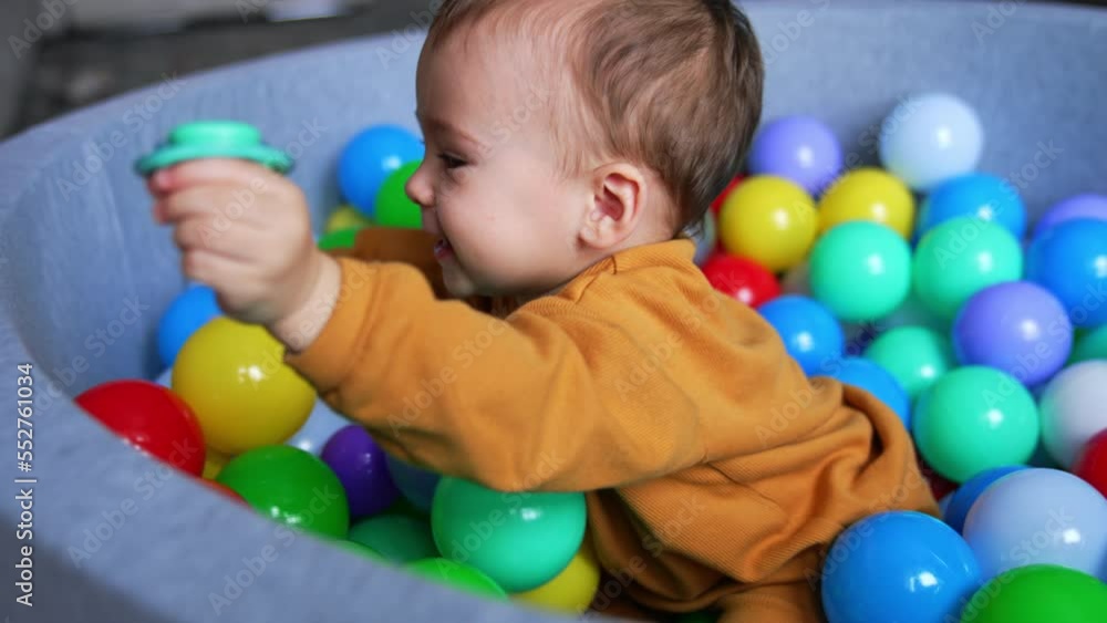 Joyful baby boy sitting in dry basin smiling adorably. Lovely child tries to climb out of the pool holding a pacifier in hand. Joyful baby boy sitting in dry basin smiling adorably. Lovely child tries to climb out of the pool holding a pacifier in hand.
