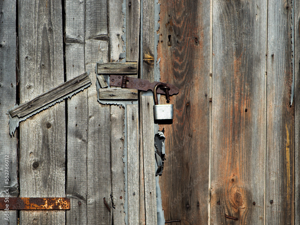 the old barn is locked with a lock hanging on the wooden door. wooden agricultural hangar. texture of old wood. the old barn is locked with a lock hanging on the wooden door. wooden agricultural hangar. texture of old wood.