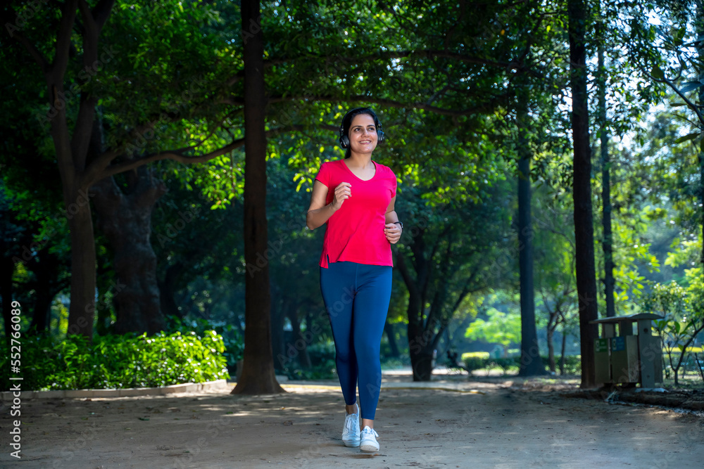 young indian woman with earphones listening music during jogging at park.