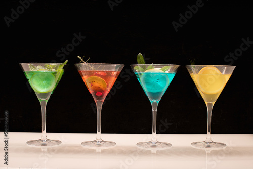 Quatre verres de différents cocktail avec des cocktails colorés sur un fond noir.