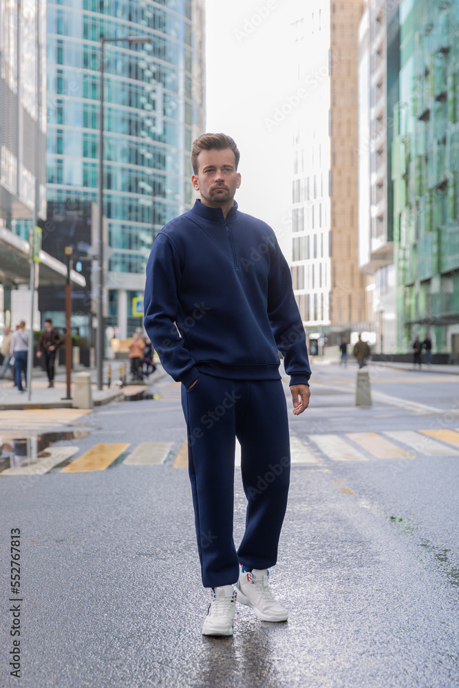 Full-length young man wears a vinous sports suit and poses for the camera. Athletic handsome young man stands on urban location and shows sports suit. Mock-up Full-length young man wears a vinous sports suit and poses for the camera. Athletic handsome young man stands on urban location and shows sports suit. Mock-up