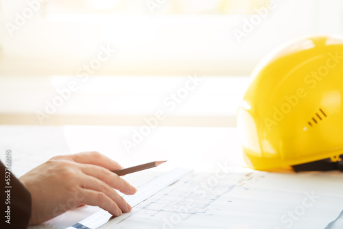 Architect working on blueprint, with architectural project at construction site at office, hard hat on engineering papers