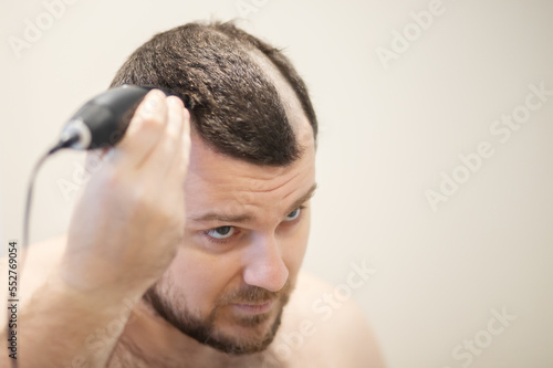 a man cuts his head with a clipper, self-shaving his head baldly photo