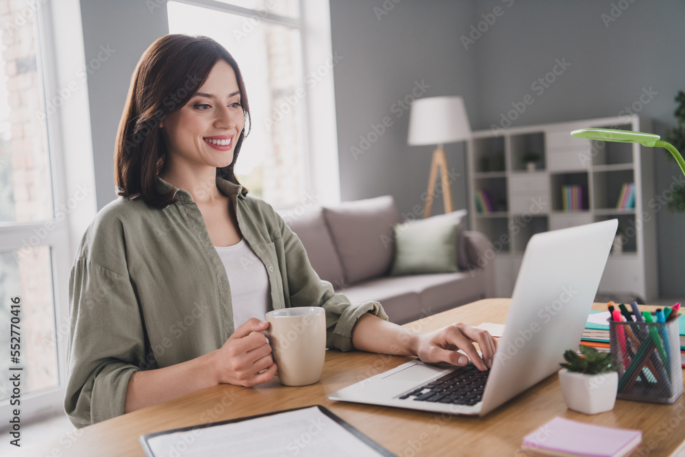 Photo of pretty positive person sitting chair arm hold fresh cacao mug typing email netbook workplace indoors Photo of pretty positive person sitting chair arm hold fresh cacao mug typing email netbook workplace indoors