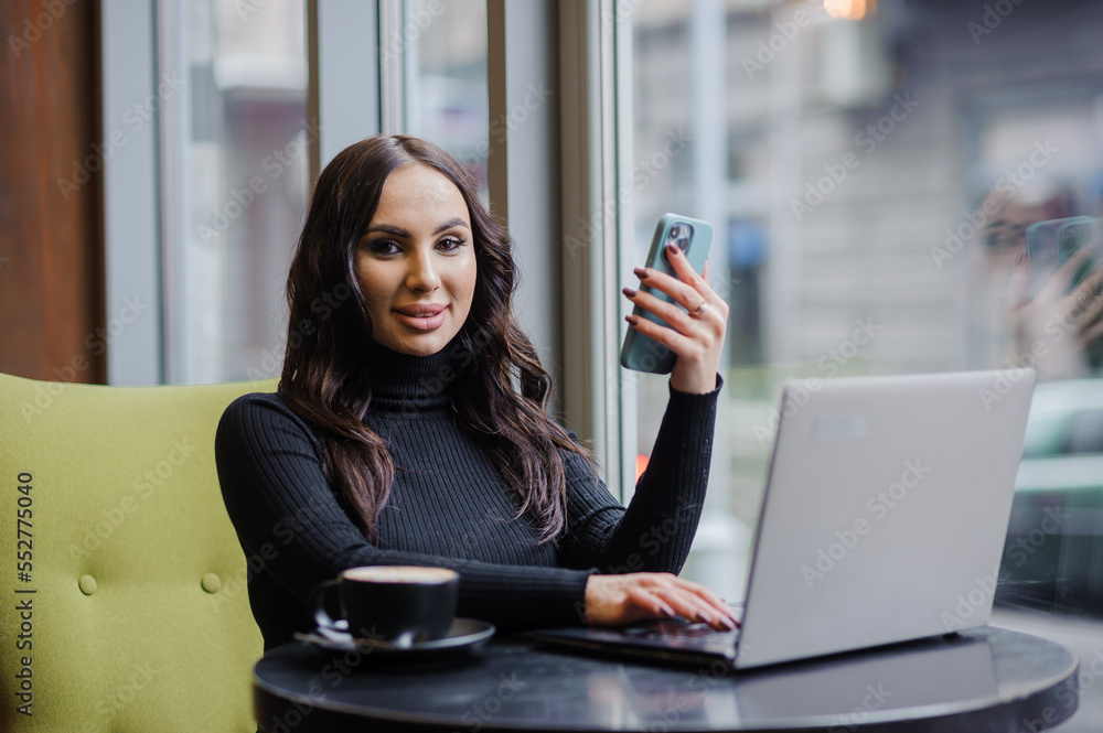 A business woman is sitting at a table in the office, talking on the phone, working on a laptop and drinking coffee A business woman is sitting at a table in the office, talking on the phone, working on a laptop and drinking coffee