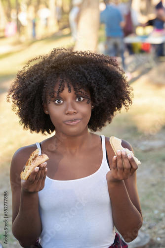 Young woman with afro hair looking at camera and smiling while enjoying having a picnic with friends outdoors in a park.