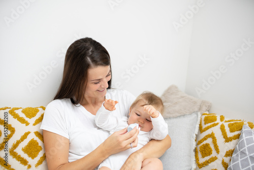 Mother lying in bed and cleans the nose of her baby with a nasal aspirator photo