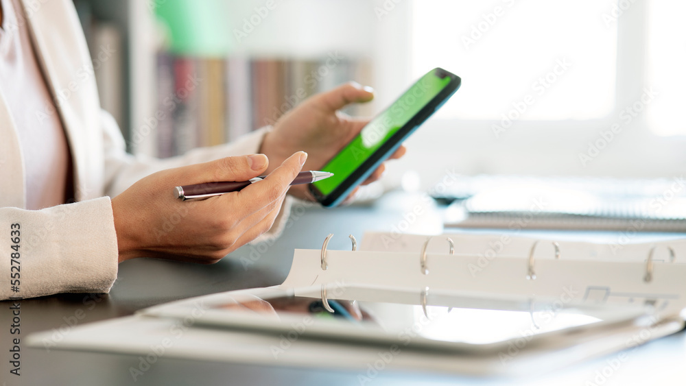 Fototapeta premium Close-up of the woman Holding Green Screen Smartphone in office Playing Game with His Thumbs.