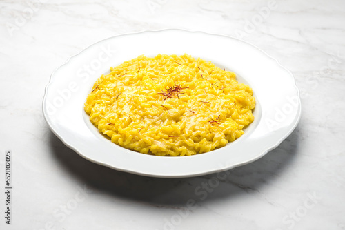Close-up of risotto alla Milanese  in a white aristocratic dish on a white marble background. A classic Lombard saffron risotto recipe. Cuisine of the north Italy, front view