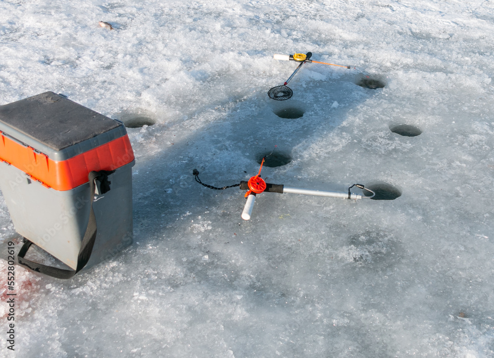 Two winter fishing rods, a net and a box for accessories lie on the ice of the lake near six holes. Winter fishing. Catching fish in winter.