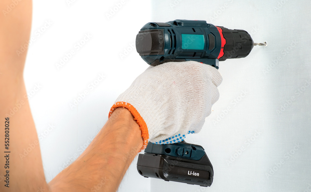 Drilling the wall with a cordless drill in protective gloves. Drilling the wall with a cordless drill in protective gloves.