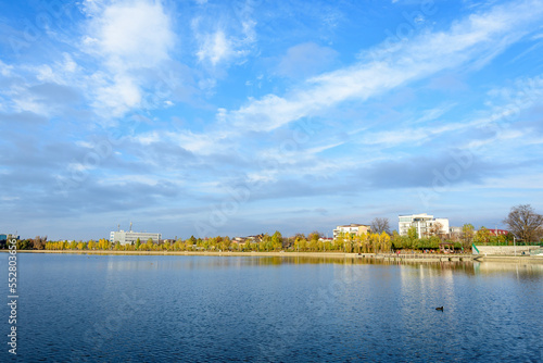 Landscape with trees and the lake in Linden Park (Parcul Tei), in Bucharest, Romania, in a sunny autumn day with white clouds and blue sky