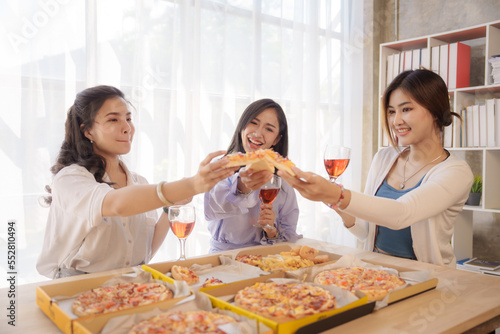 Group of young asian office girl friends having fun and celebrating pizza on table during party