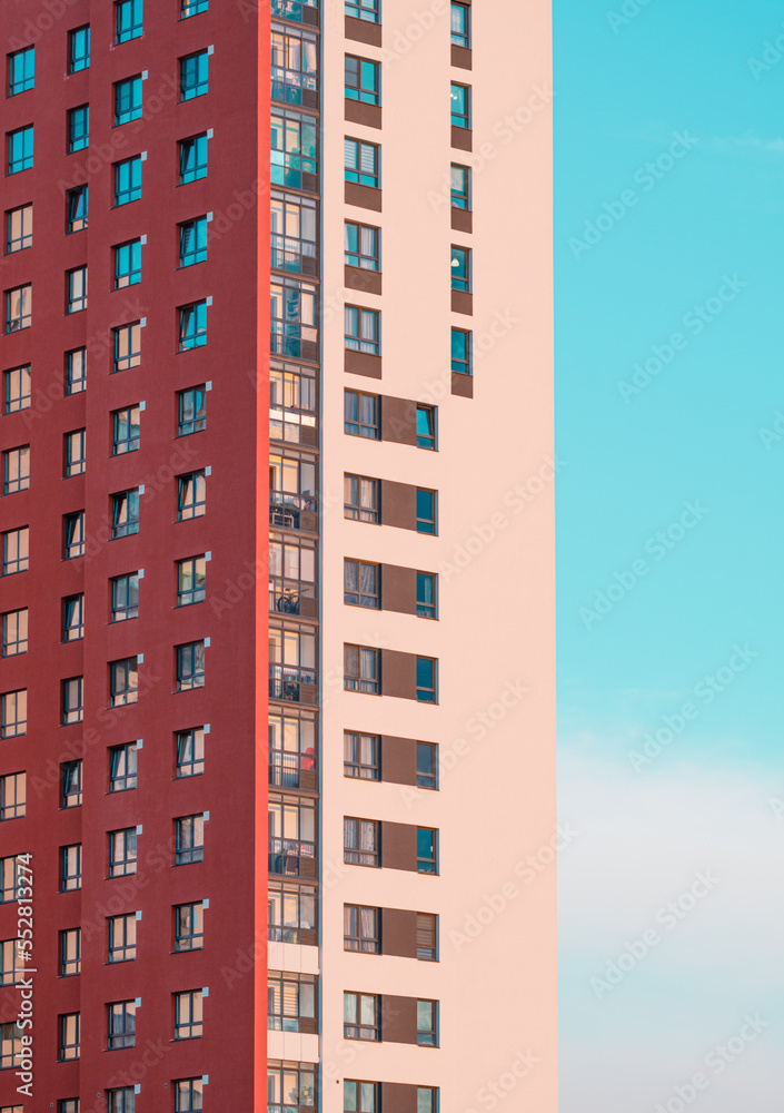 A red and beige apartment building on a blue sky background. Sunset rays of the sun