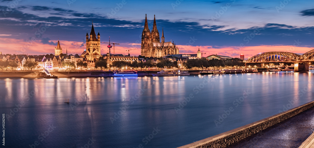 Panorama of illuminated Cologne or Koln Cathedral Dom and bridge over Rhine river in the twilight after sunset
