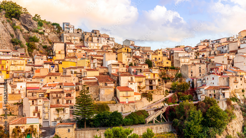 old mediterranean mountain dense town with levels of yellow houses and terraces on a steep mountain in evening light, vintage european village on a rock